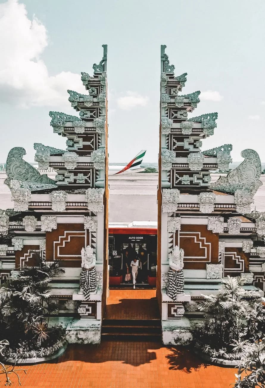 Porte balinaise sculptée devant le tarmac de l'aéroport Ngurah Rai de Bali, avec un avion de ligne en arrière-plan