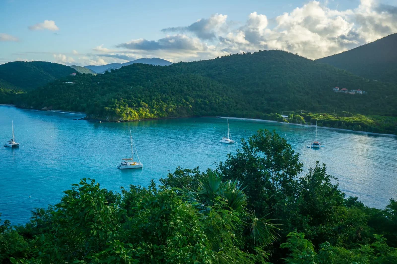 Baie turquoise bordée de collines couvertes de jungle avec des bateaux au mouillage, vue depuis un point haut de la côte, comme au viewpoint de Jemeluk à Amed