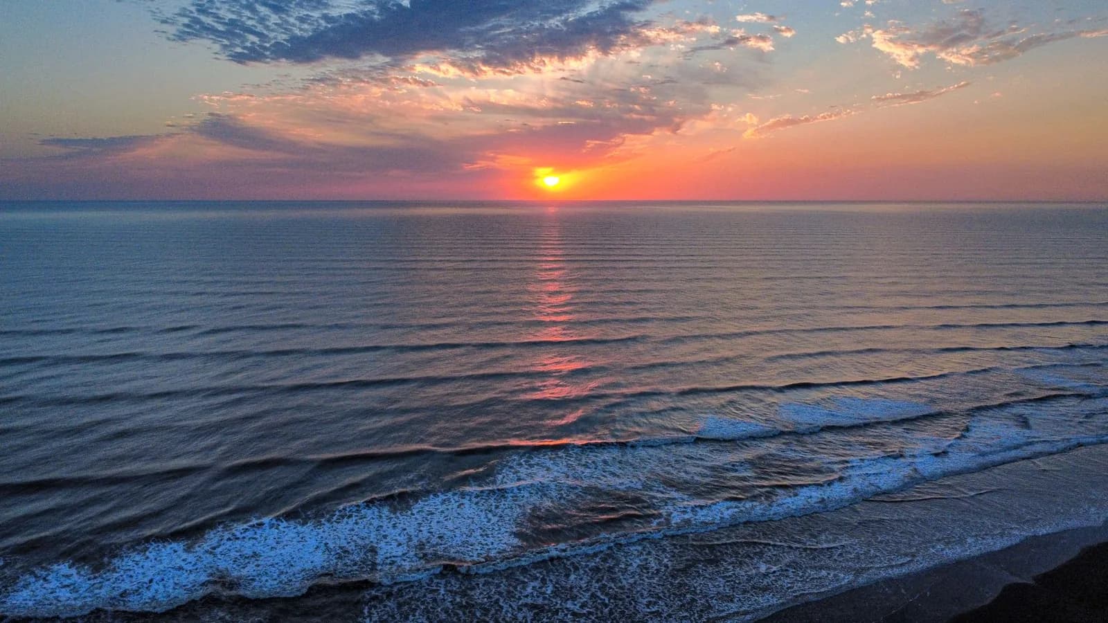 Soleil levant au ras de l'horizon au-dessus d'une mer calme, vue depuis la plage, comme sur la côte est de Bali à Amed