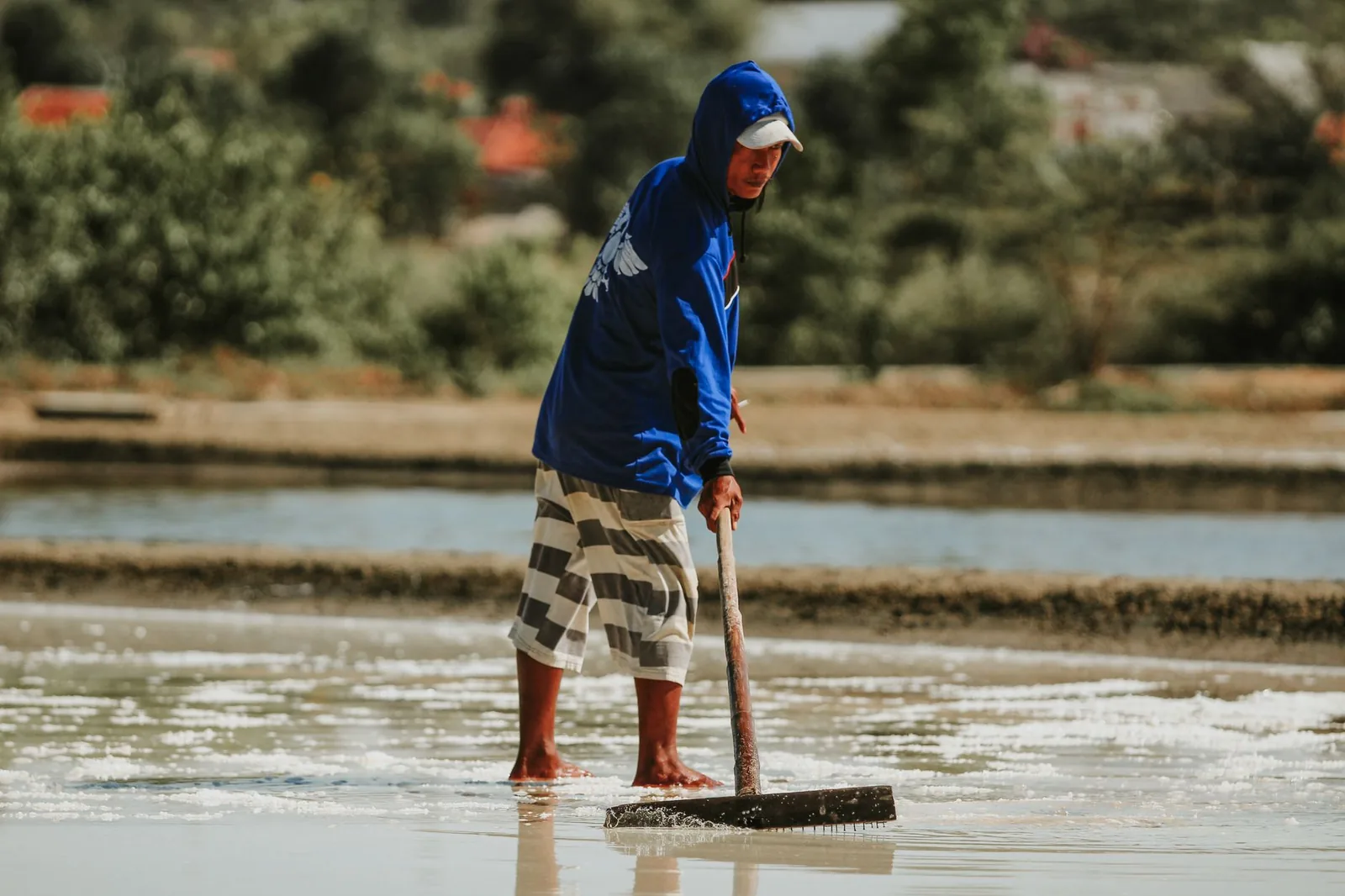 Producteur de sel indonésien raclant un bassin d'évaporation d'eau de mer, comme dans les salines artisanales d'Amed à Bali
