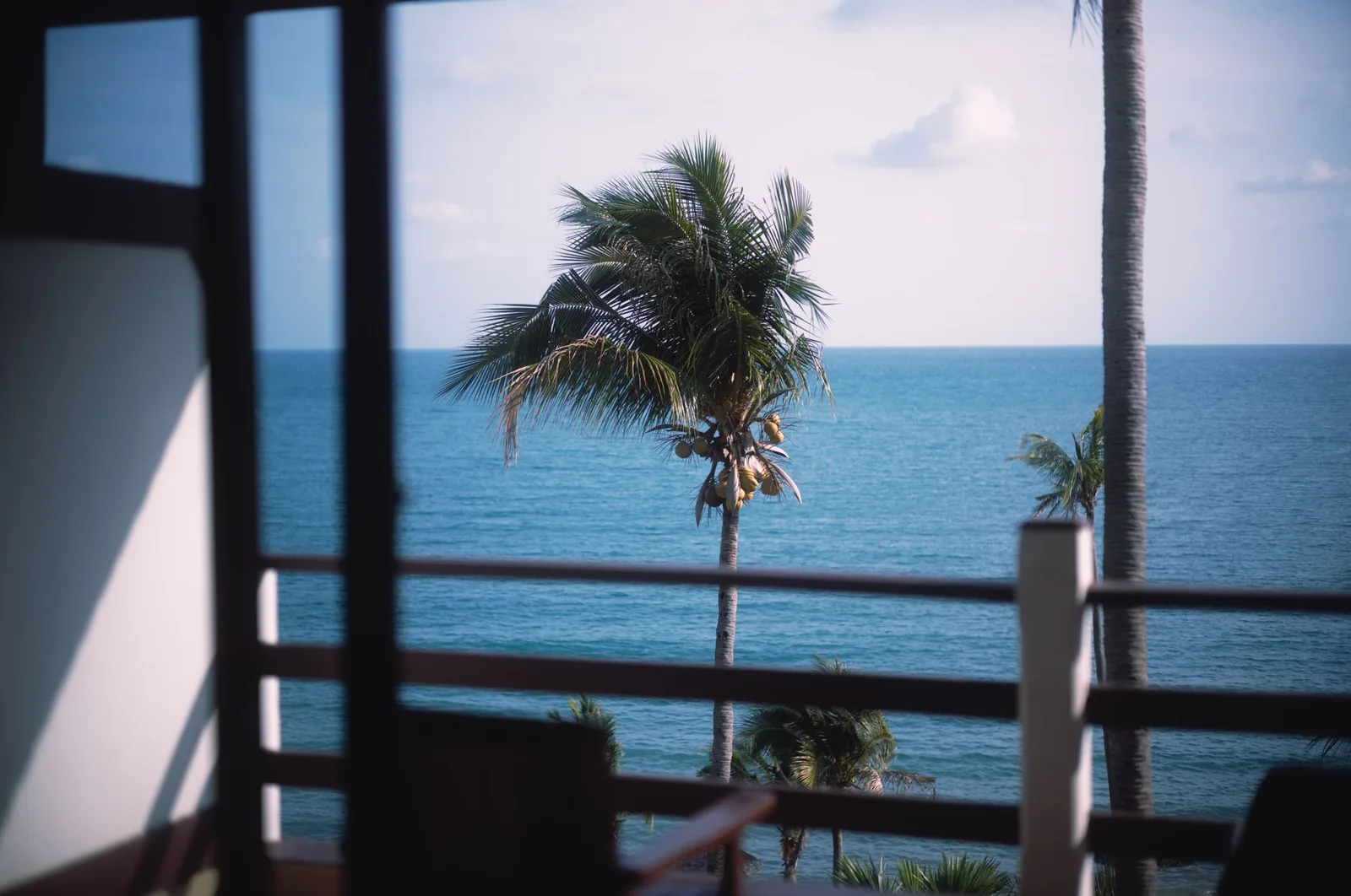Vue sur la mer et un cocotier depuis le balcon en bois d'une chambre d'hôtel tropicale, comme dans les hébergements de la côte d'Amed à Bali