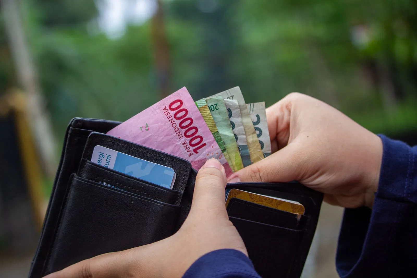 Mains sortant des billets de roupies indonésiennes d'un portefeuille, dont un billet de 100 000 IDR, à Bali