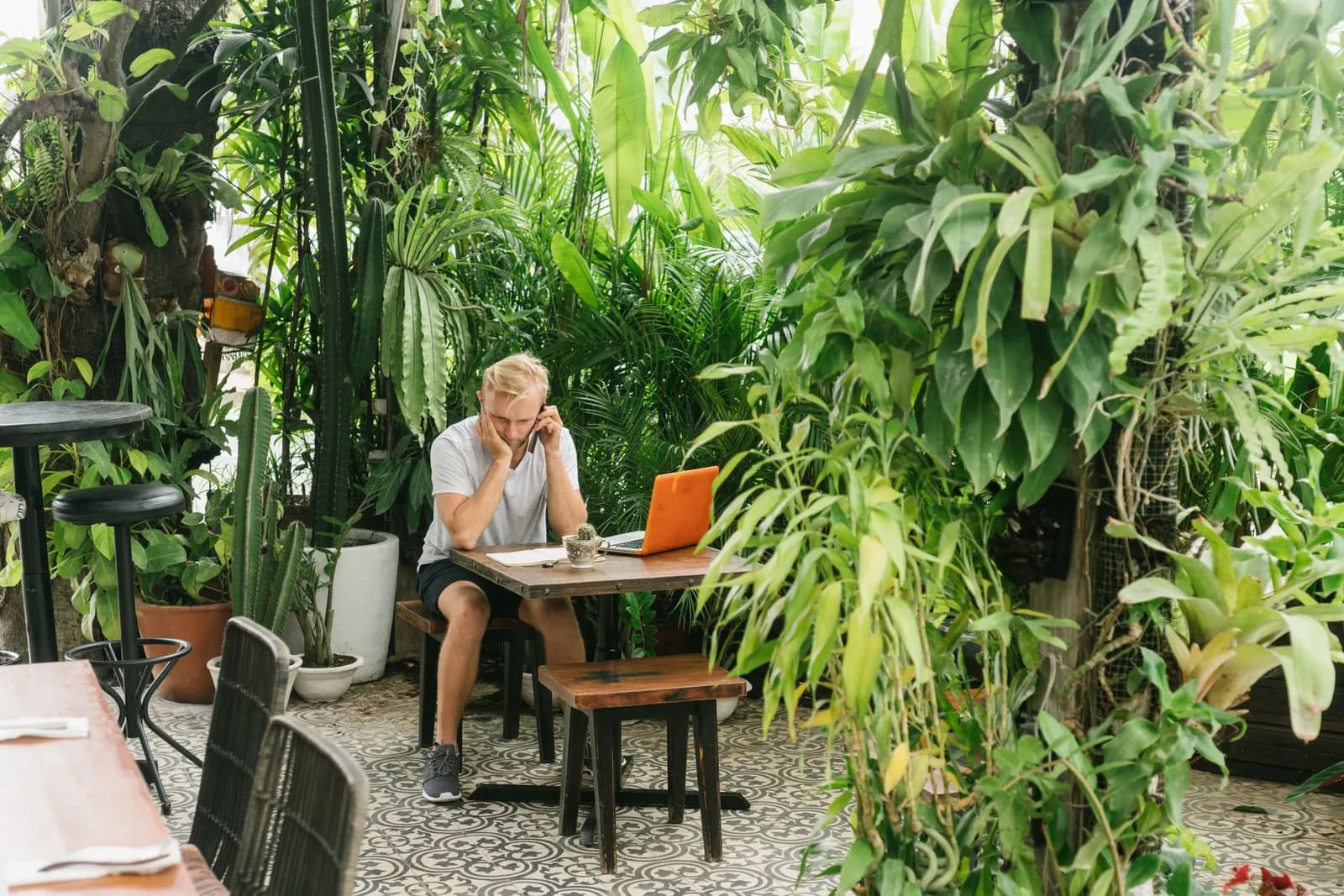 Homme travaillant sur un ordinateur portable à la table d'un café-jardin tropical, dans le style des adresses de télétravail de Canggu à Bali