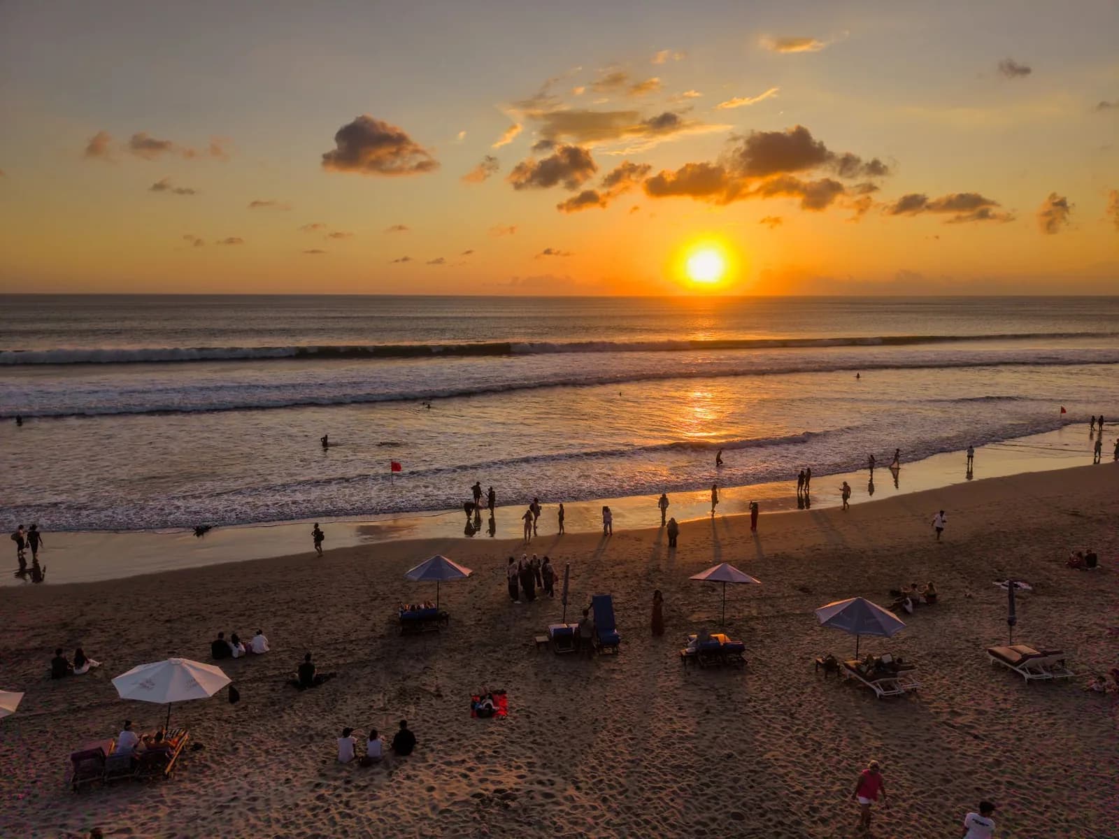 Coucher de soleil sur une plage de la côte ouest de Bali, transats et parasols sur le sable, promeneurs au bord de l'eau