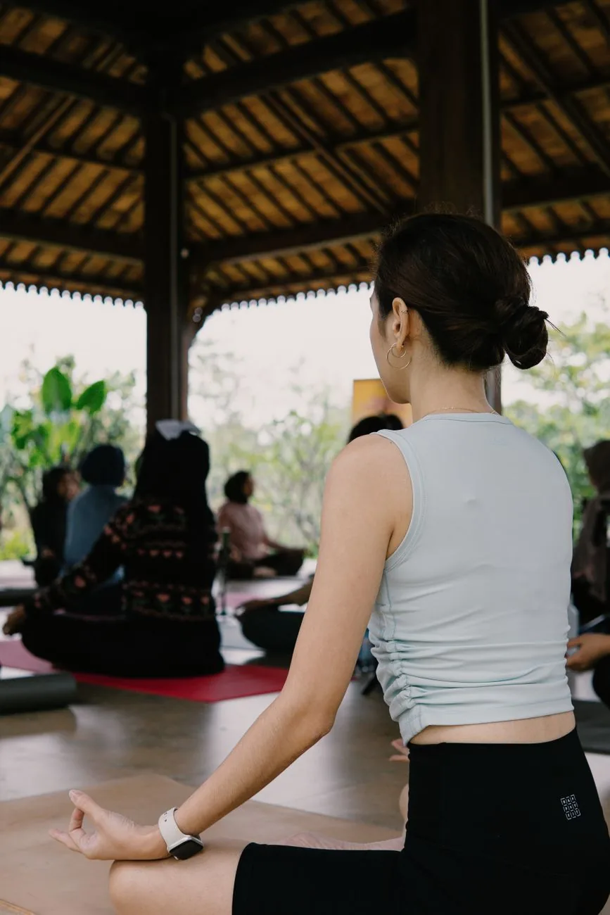 Cours de yoga collectif assis en tailleur sous un pavillon en bois ouvert sur la végétation, en Indonésie