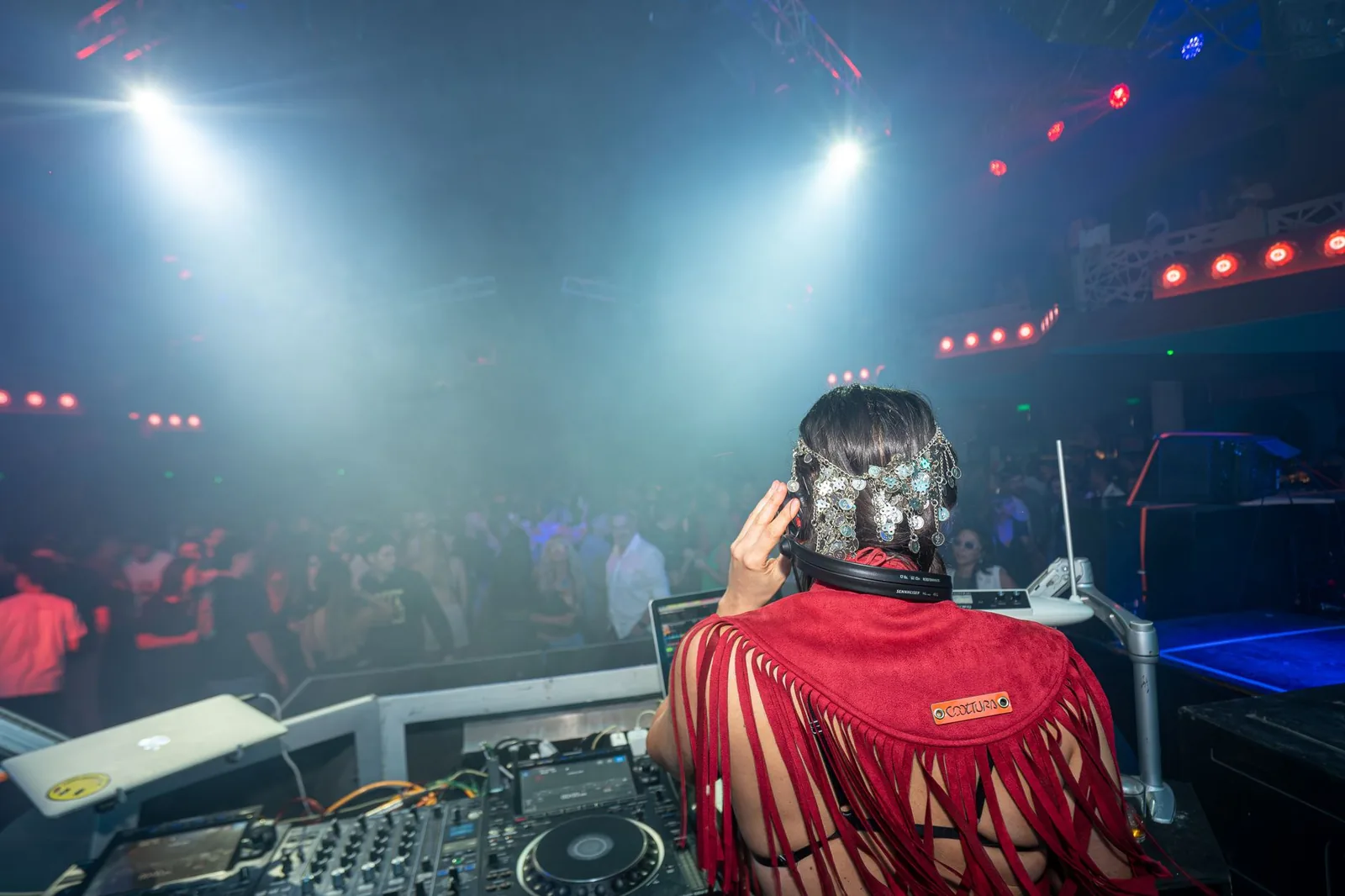 DJ vu de dos derrière ses platines face à une piste de danse noyée de fumée et de lumières colorées