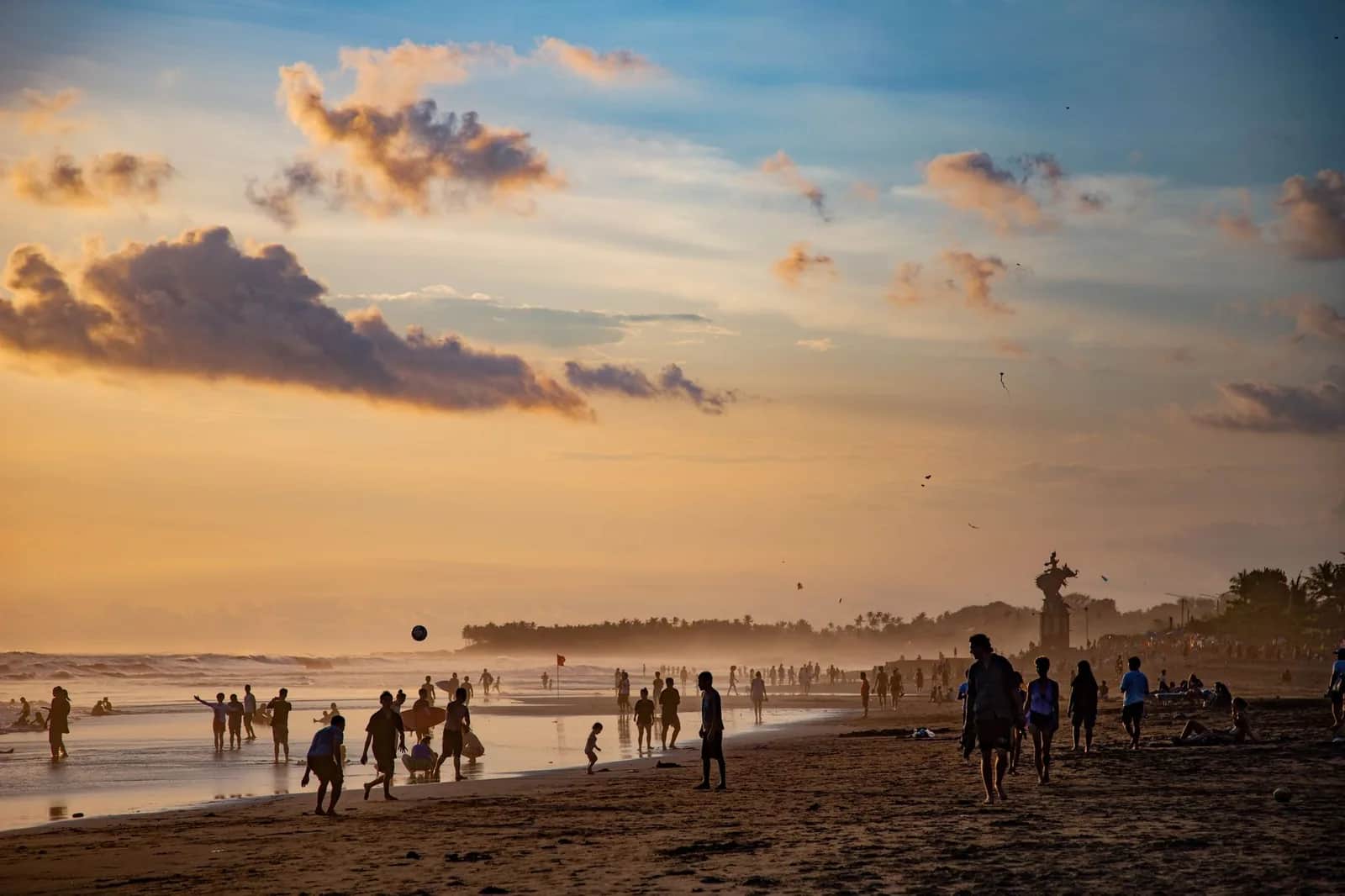 Plage de Canggu à Bali au coucher du soleil, silhouettes de baigneurs et de surfeurs sur le sable volcanique sombre, sanctuaire balinais en arrière-plan