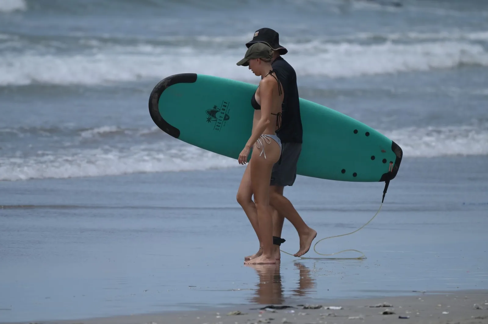 Deux surfeurs marchent sur le sable avec une planche en mousse d'école de surf, sur une plage de Bali