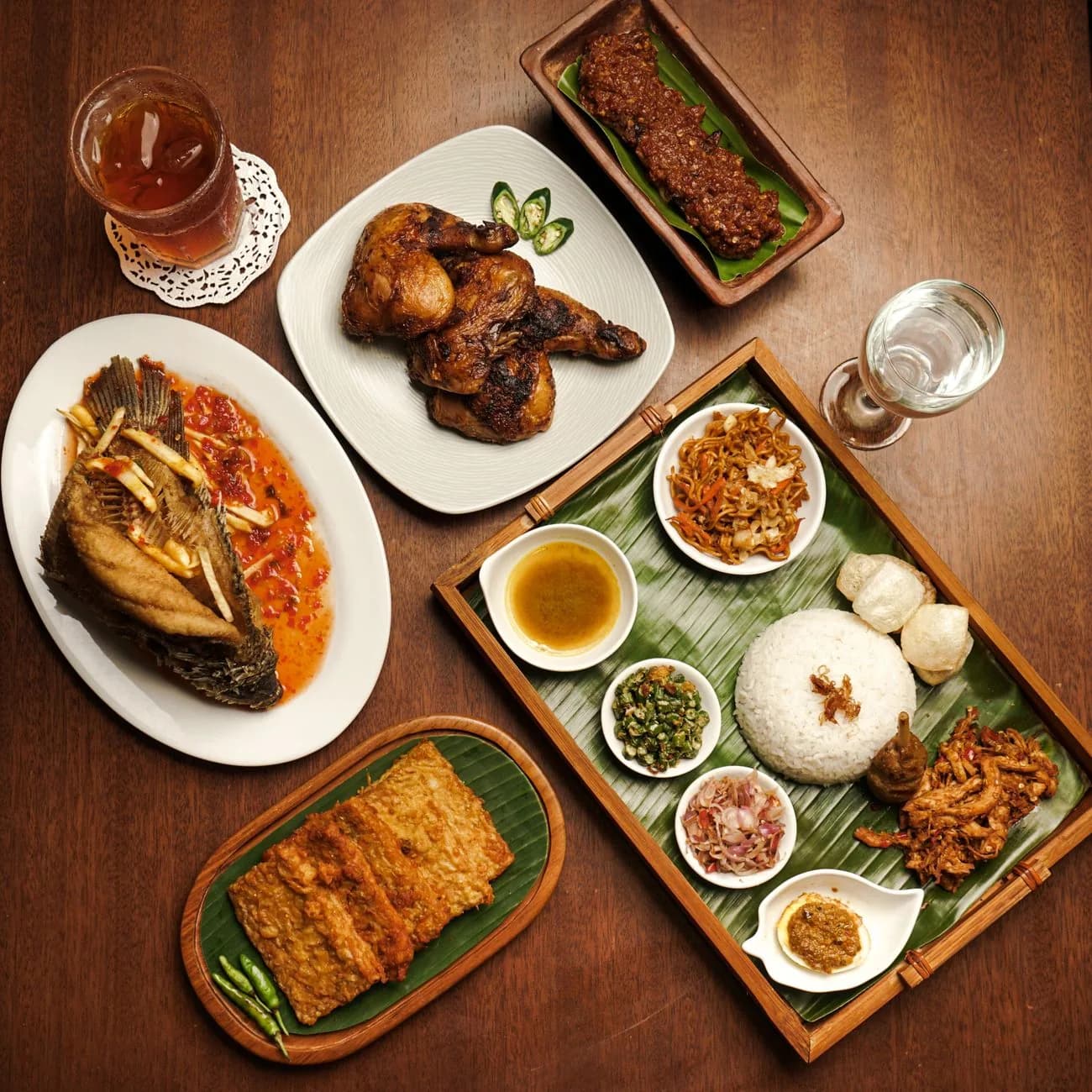Repas indonésien servi sur une table en bois, poisson grillé, riz sur feuille de bananier, sambal et accompagnements