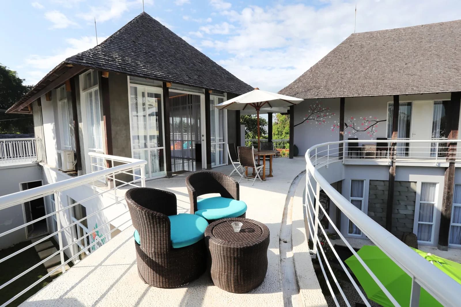 Terrasse d'une guesthouse balinaise moderne avec fauteuils en rotin et toit de bardeaux, typique des hébergements de Canggu à Bali