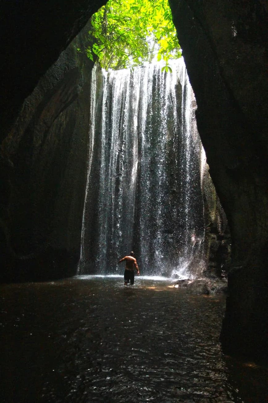 Baigneur marchant dans le bassin au pied d'une cascade encaissée à Bali