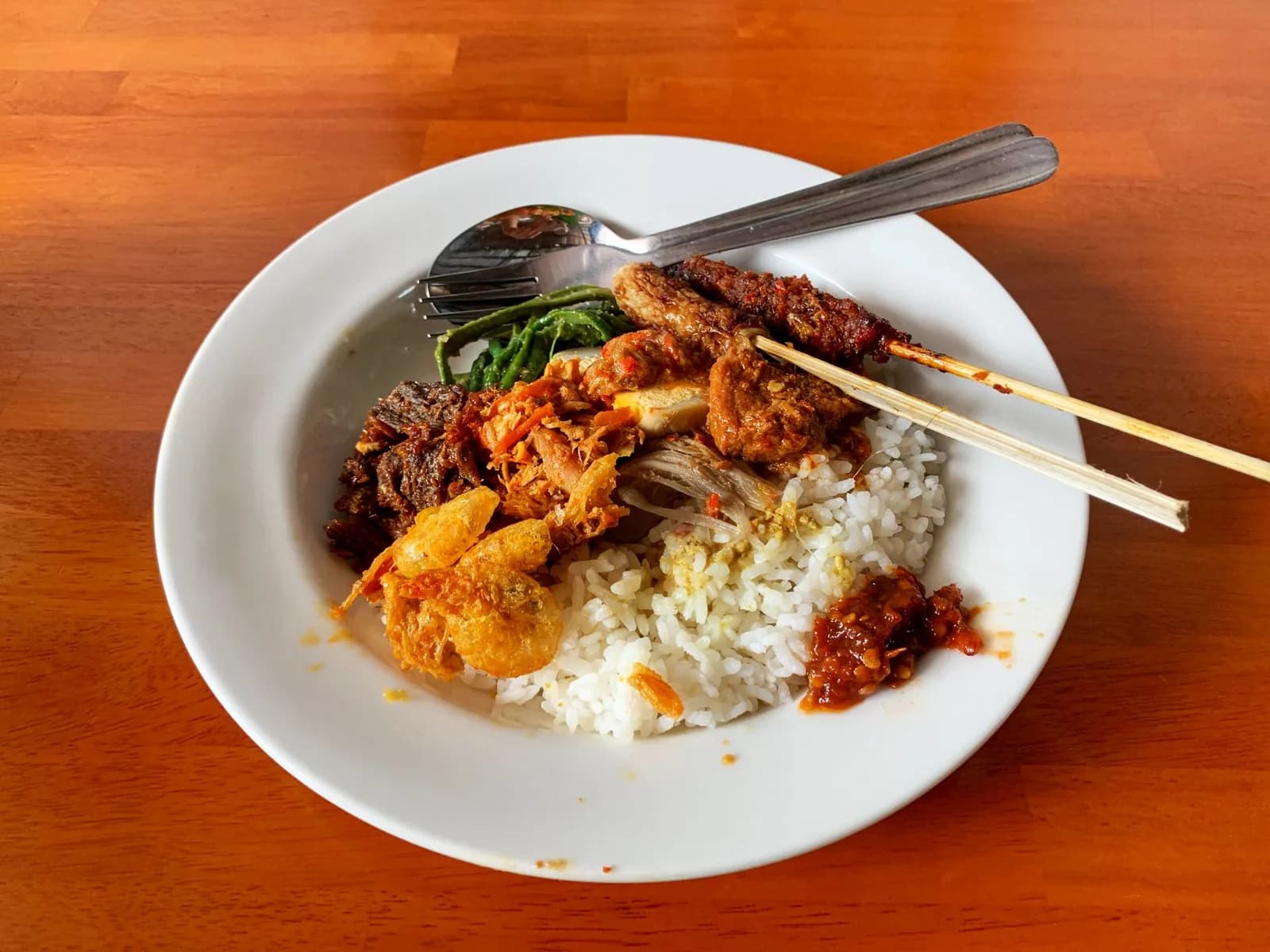 Assiette de nasi campur servie dans un warung à Bali : riz blanc, brochette de satay, lawar, tempeh, œuf, kerupuk et cuillerée de sambal rouge