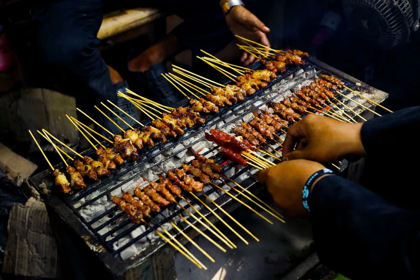 Vendeur de rue indonésien retournant des dizaines de brochettes de satay sur un gril à braises, la nuit, sur un marché nocturne