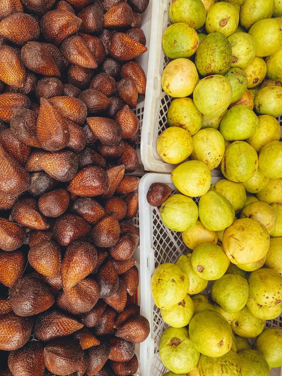 Étal de marché en Indonésie avec des cageots de salak, le fruit serpent à peau écailleuse brune, à côté de goyaves vertes