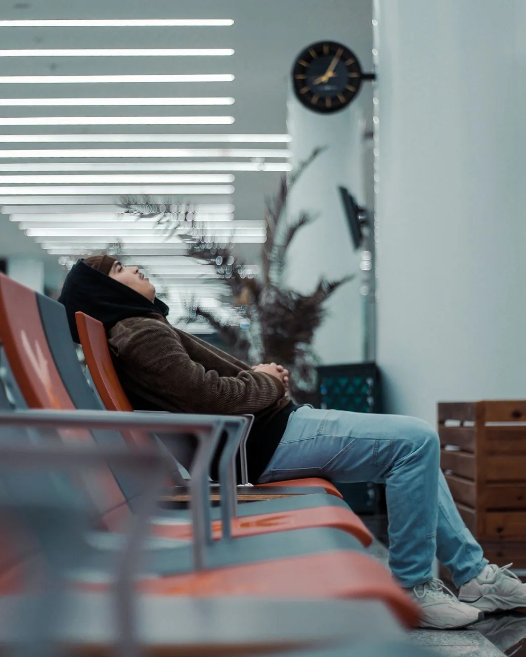 Voyageur endormi sur un siège de salle d'embarquement pendant une escale, sous l'horloge du terminal
