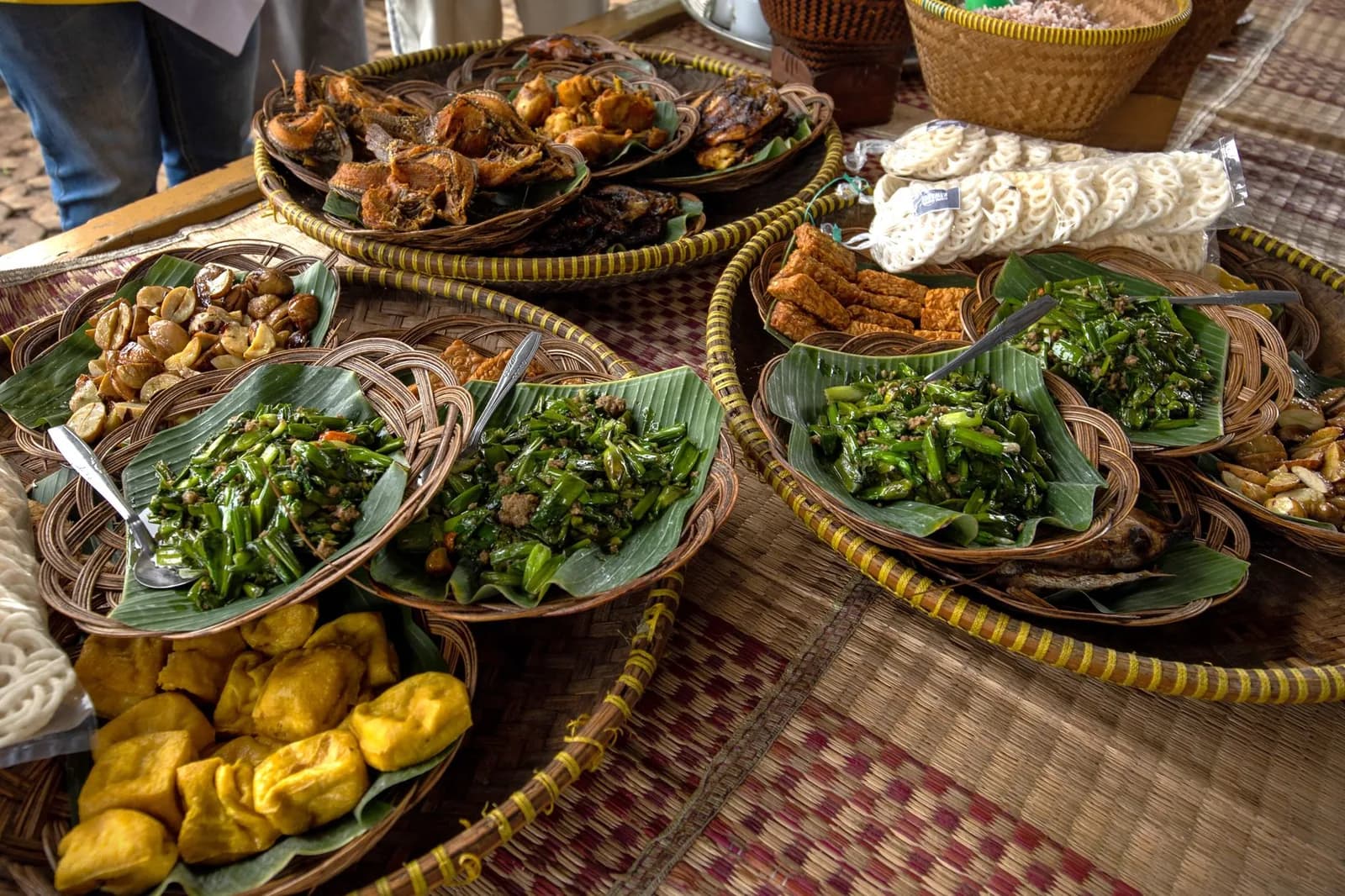Corbeilles de plats indonésiens sur feuilles de bananier : légumes sautés, tofu frit, brochettes et crackers