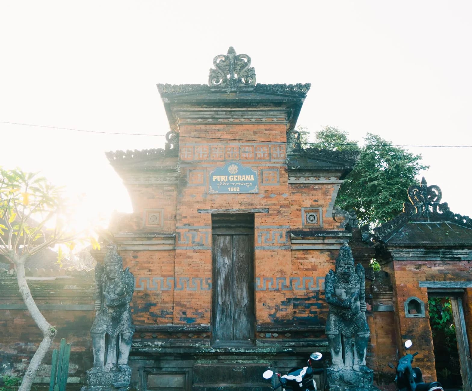 Portail en brique rouge d'un temple balinais, gardé par deux statues, à contre-jour