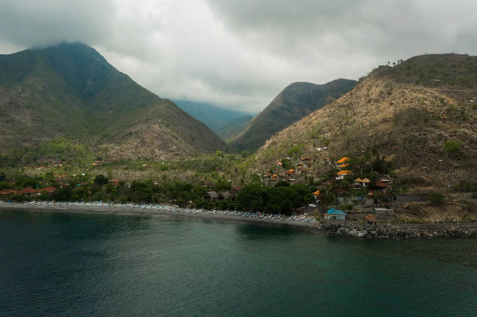 Vue aérienne de la baie d'Amed, jukungs alignés sur la plage de galets noirs et collines de l'est de Bali