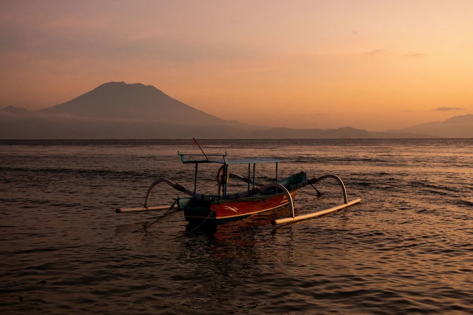 Jukung, bateau traditionnel à balancier, au coucher du soleil avec le volcan Agung à l'horizon