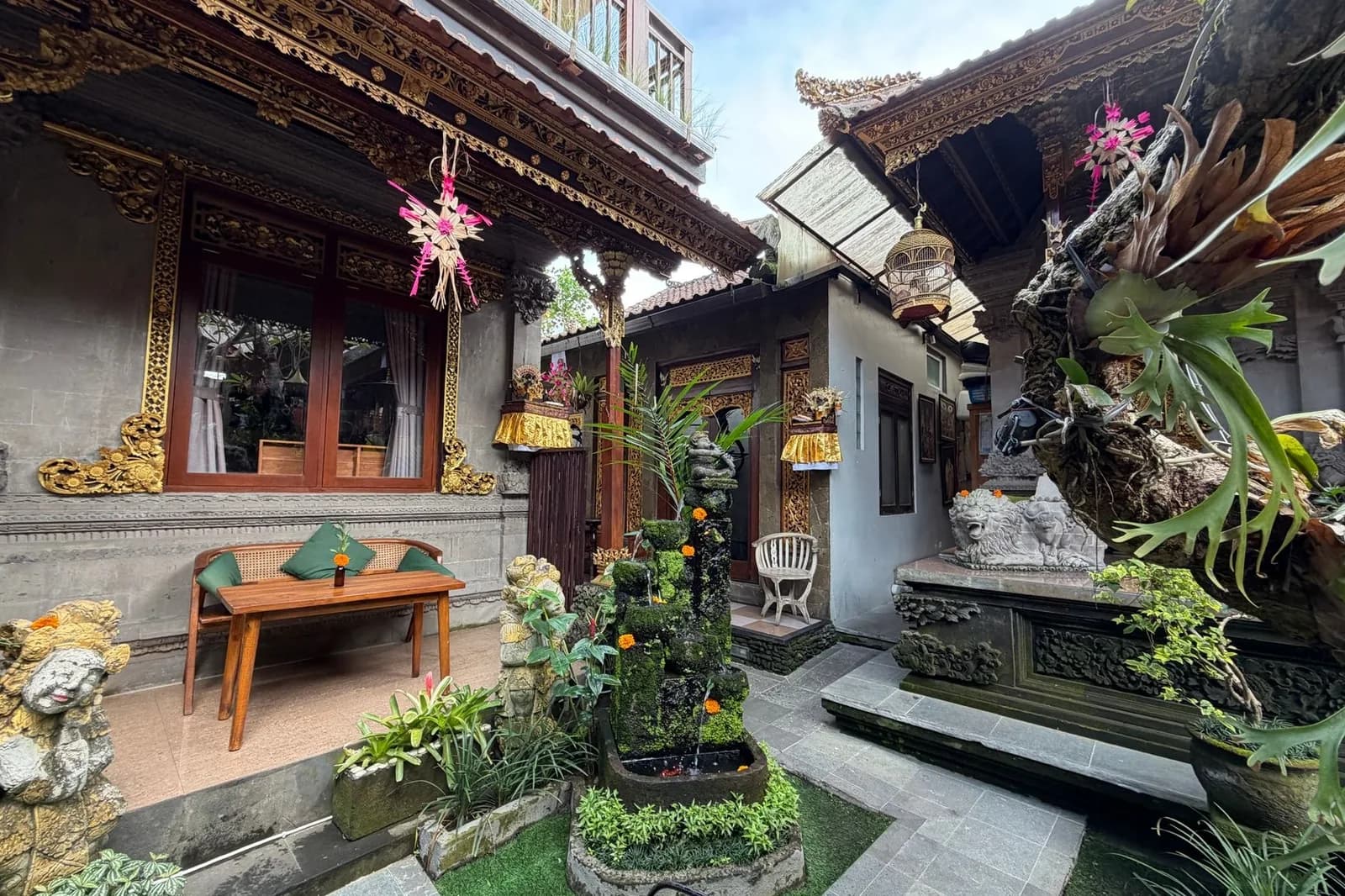 Cour d'un homestay balinais aux boiseries sculptées, statues et plantes tropicales