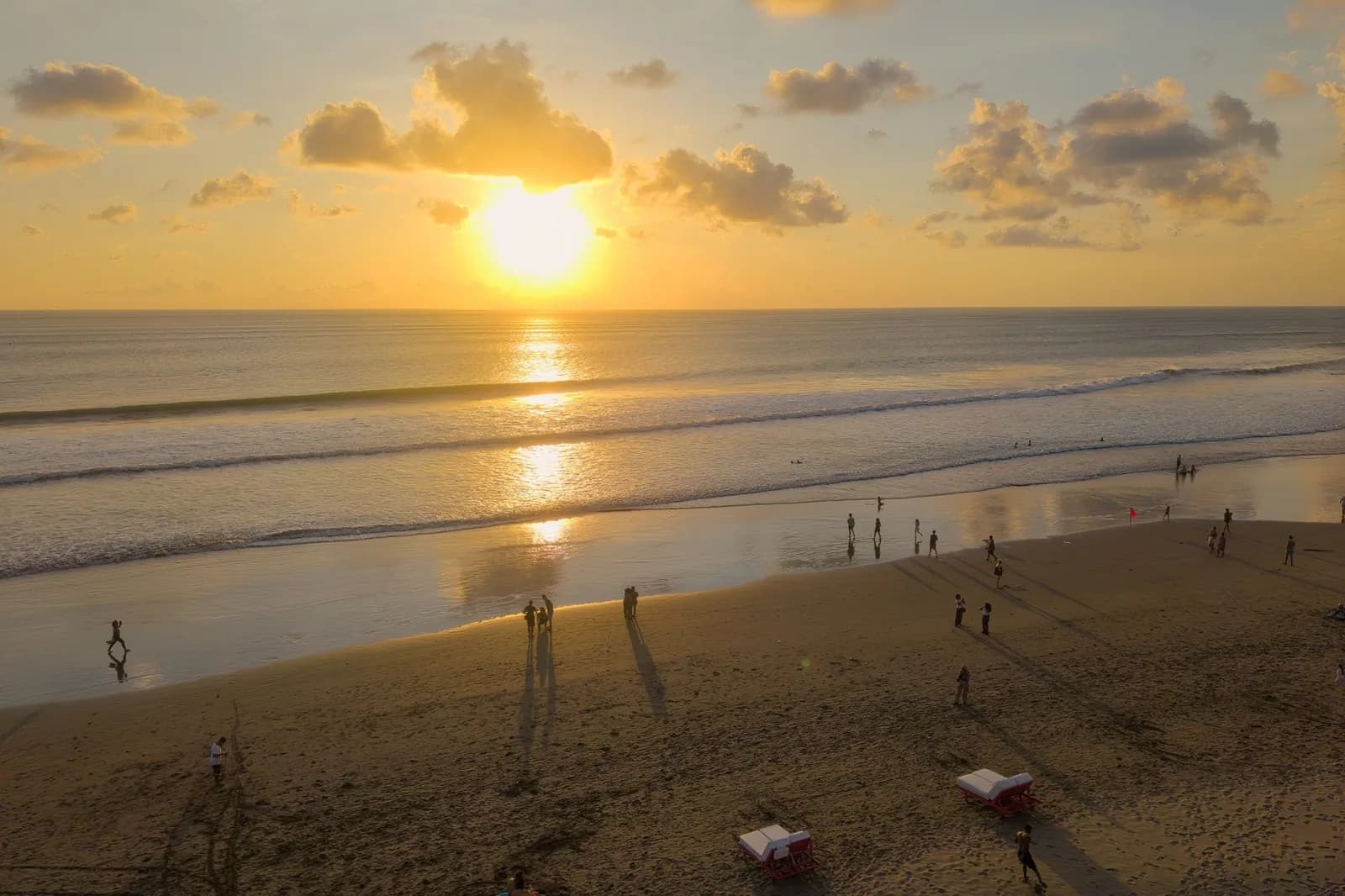 Coucher de soleil sur la plage de Seminyak, sable sombre humide et promeneurs au bord de l'eau