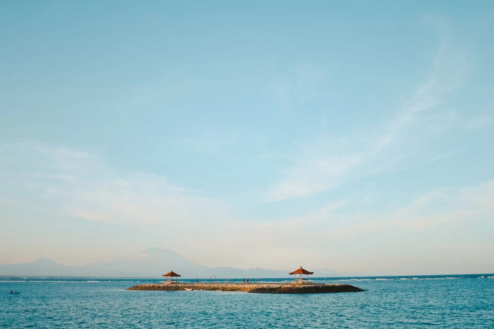 Mer calme à Sanur, pavillons balinais sur un îlot et volcan au loin