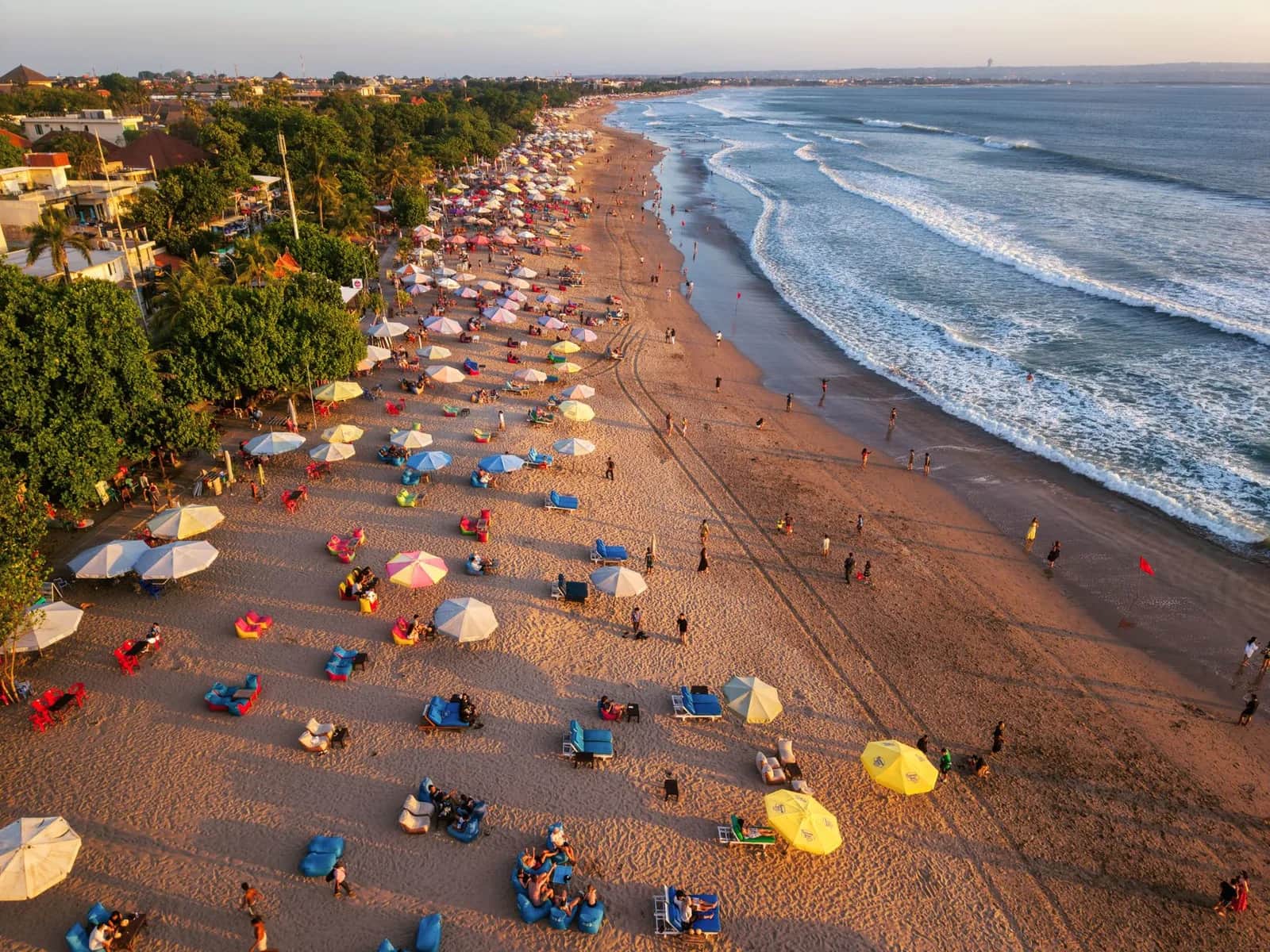Vue aérienne de la plage de Kuta à Bali au coucher du soleil, parasols et transats devant les hôtels