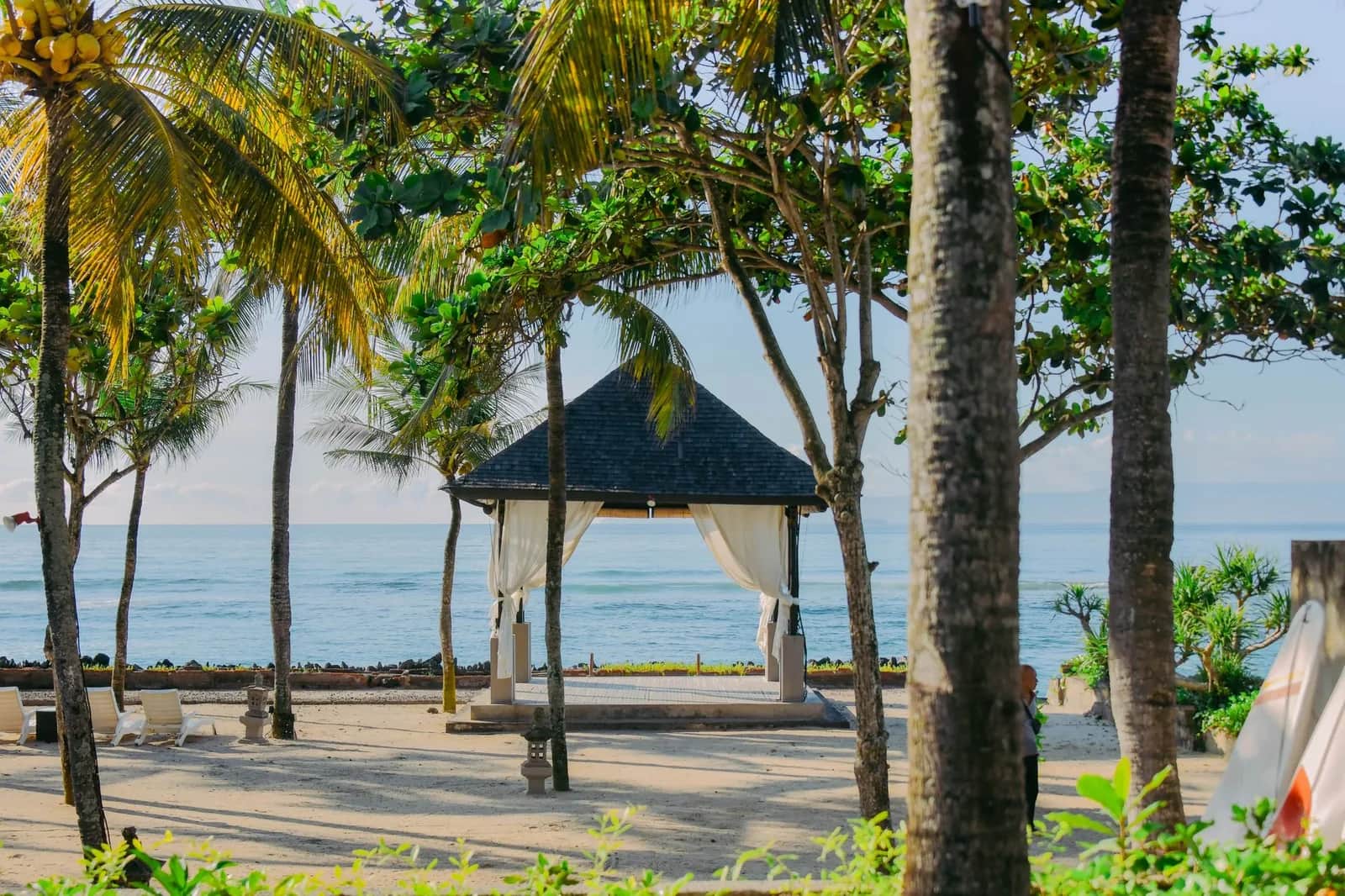 Pavillon de plage aux voilages blancs entre les cocotiers, face à une mer calme du sud de Bali