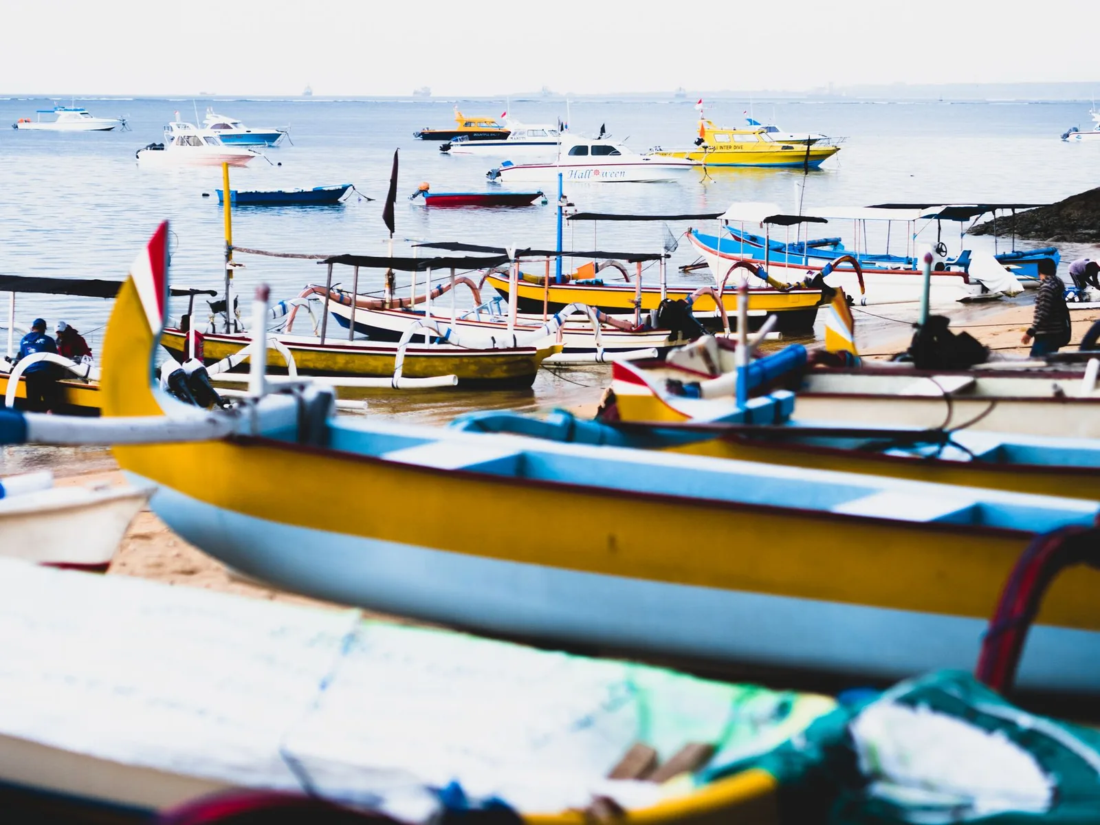 Jukung colorés échoués sur la plage de Sanur, avec des bateaux de plongée au mouillage dans le lagon, Bali