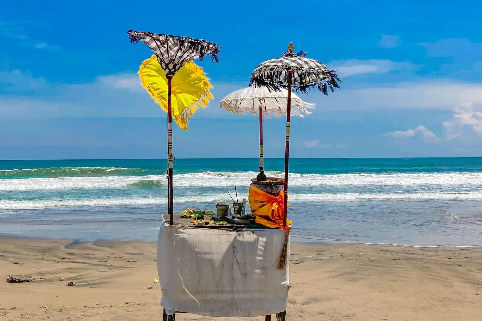 Offrandes et parasols cérémoniels balinais sur le sable d'une plage du sud-ouest de Bali, vagues turquoise derrière