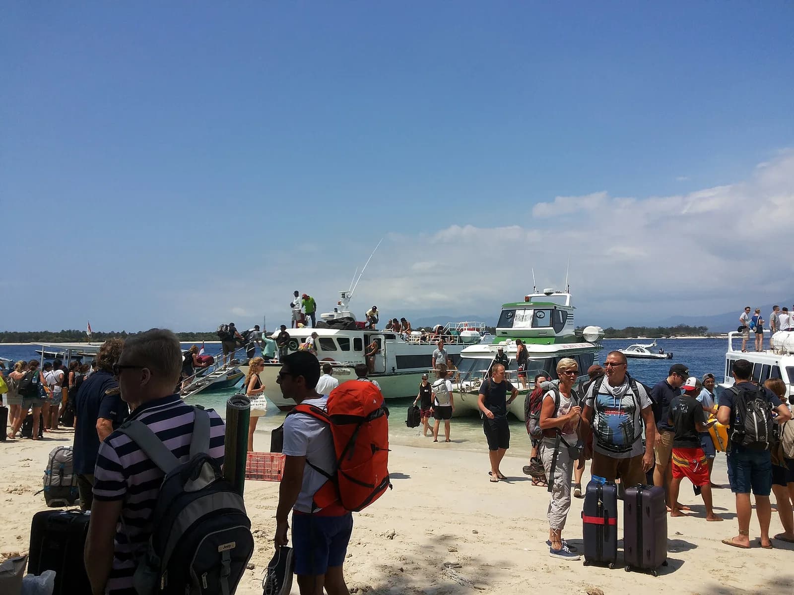 Passagers avec sacs à dos et valises débarquant des fast boats échoués sur la plage de Gili Trawangan