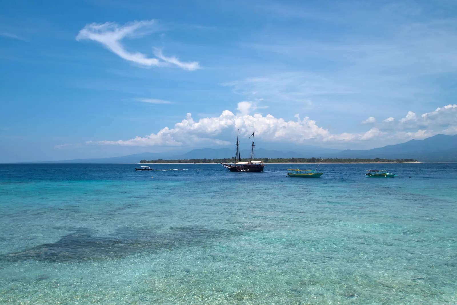 Gili Air vue depuis Gili Meno, avec le récif visible sous l'eau transparente et le massif du Rinjani sur Lombok à l'arrière-plan
