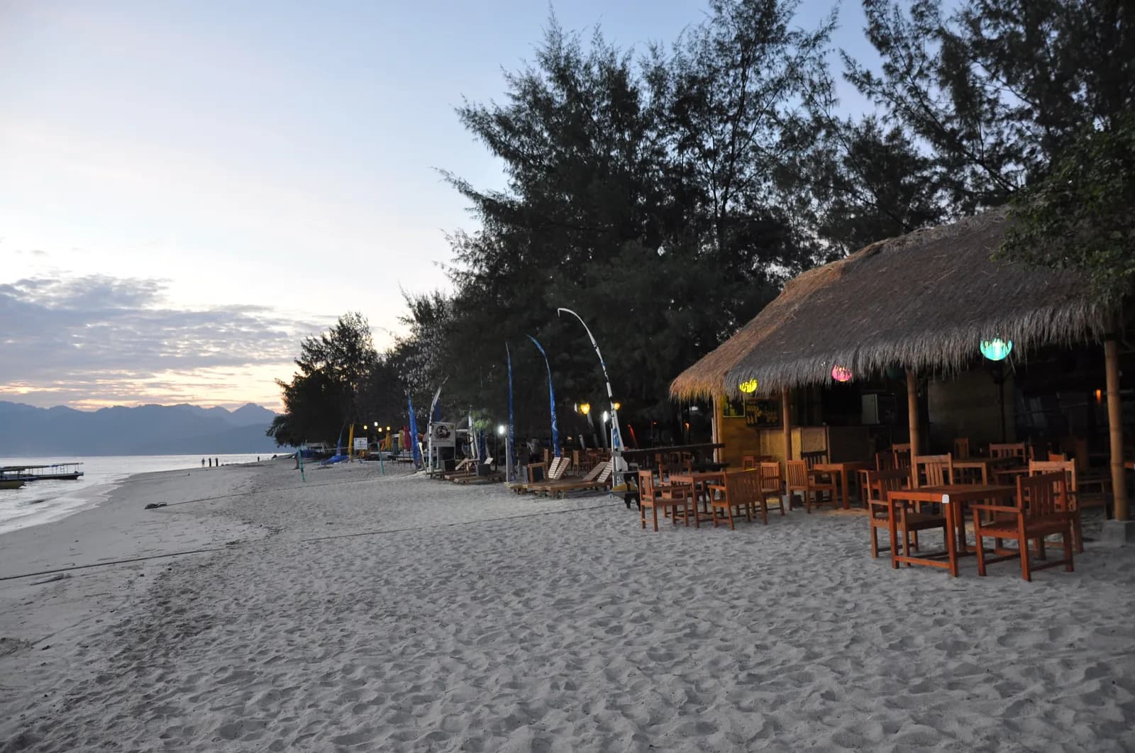 Restaurants de plage aux toits de chaume et tables posées dans le sable sur le front de mer de Gili Trawangan, au crépuscule