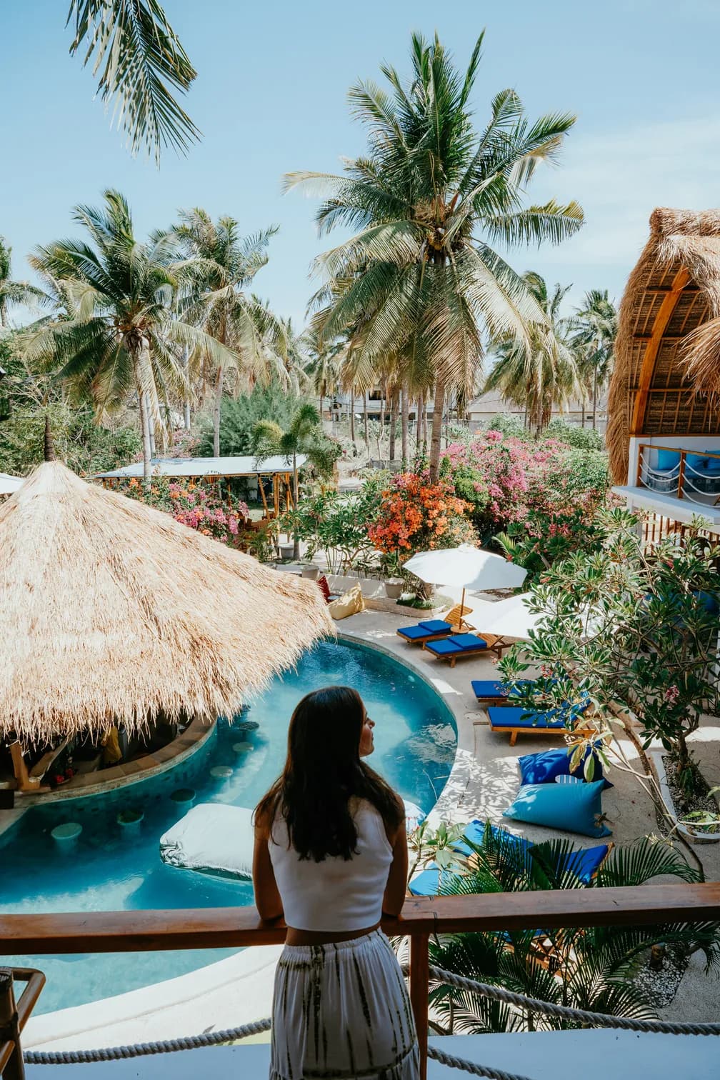 Piscine, transats et bungalows aux toits de chaume dans un hébergement de Gili Trawangan, entouré de cocotiers et de bougainvilliers