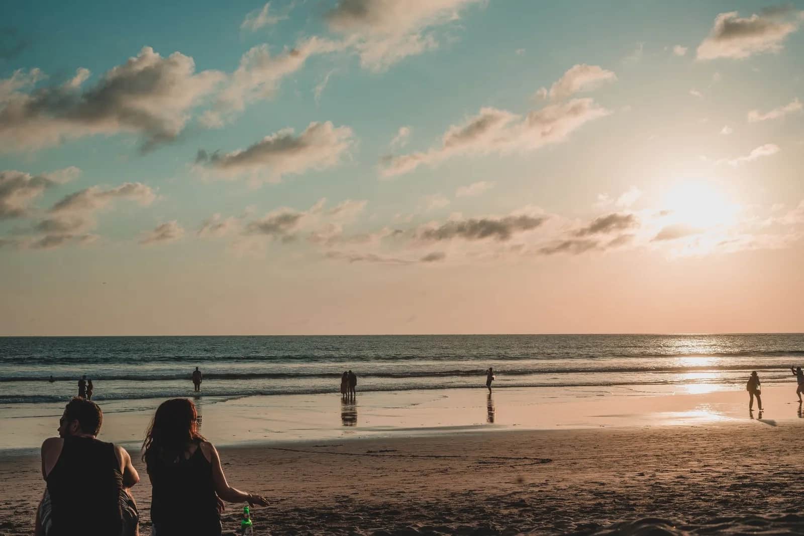 Plage large de la baie de Jimbaran au coucher du soleil, promeneurs sur le sable mouillé, sud de Bali