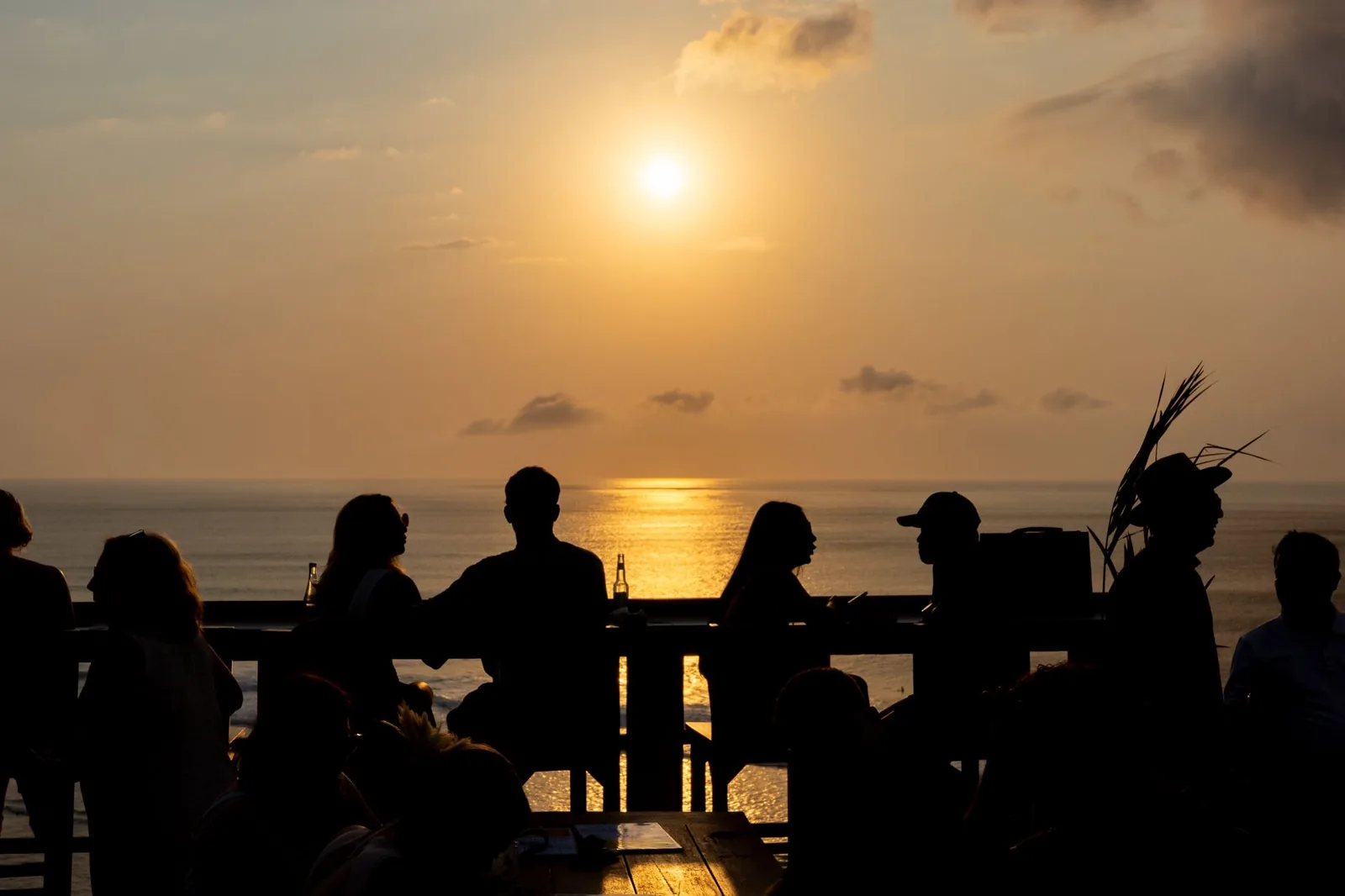 Silhouettes de clients attablés dans un bar face à l'océan au coucher du soleil, comme sur le front de mer de Kuta à Bali