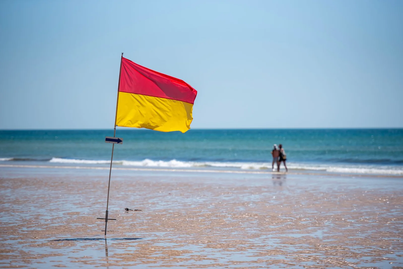 Drapeau rouge et jaune planté sur le sable mouillé et baigneurs au bord de l'eau, comme dans la zone de baignade surveillée par les sauveteurs de la plage de Kuta à Bali
