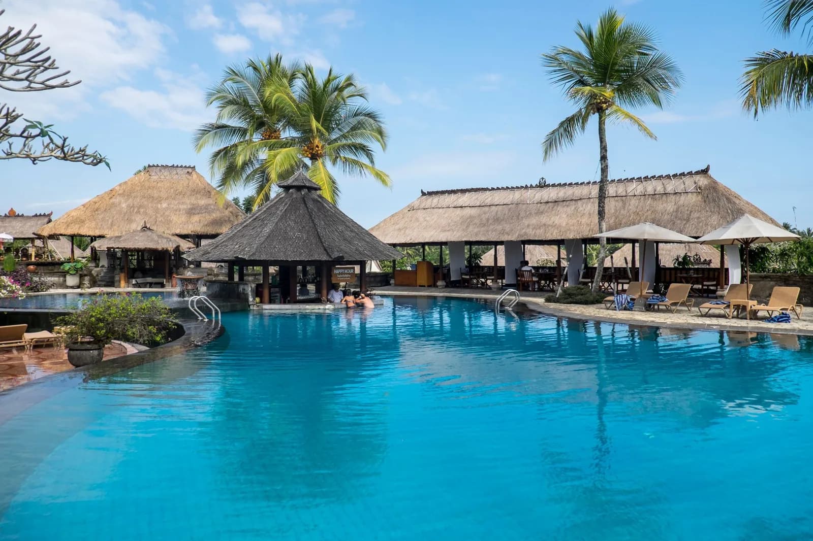 Piscine d'un hôtel balinais bordée de palmiers et de pavillons aux toits de chaume, comme dans les hôtels de Kuta et Legian