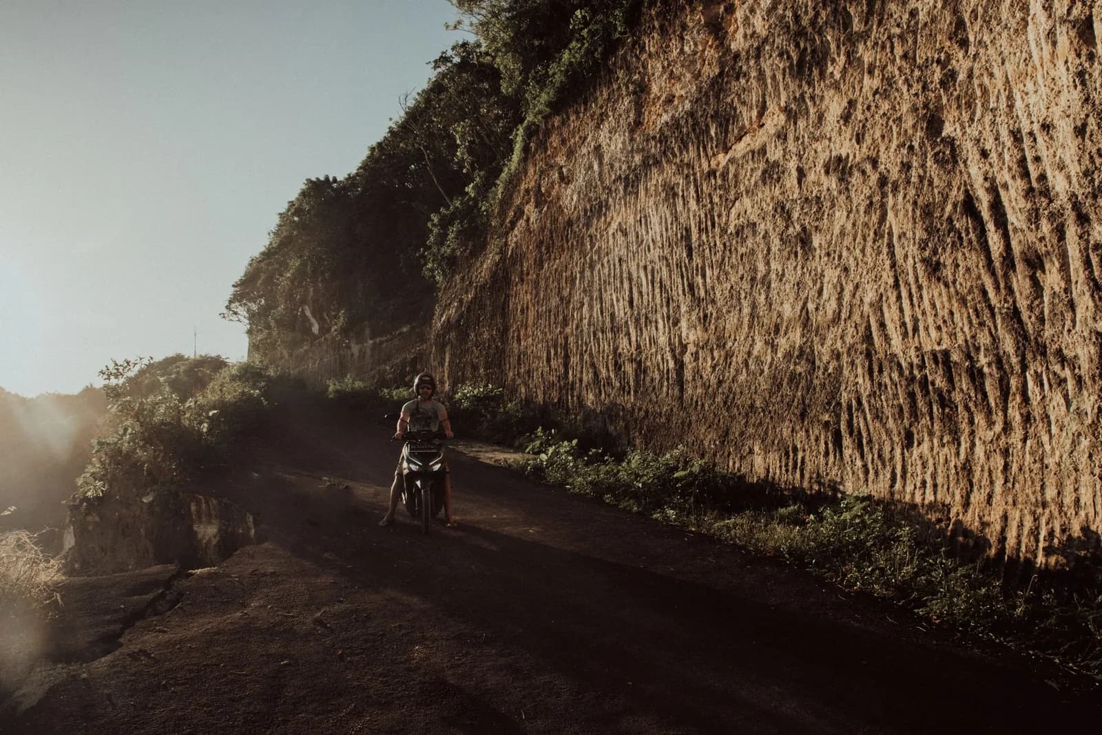 Scooter remontant une piste de terre taillée dans une falaise du sud de Bali au coucher du soleil