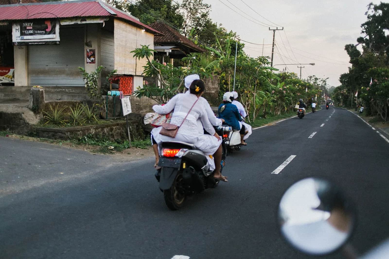 Scooters roulant sur une route de village bordée d'échoppes à Bali, en Indonésie
