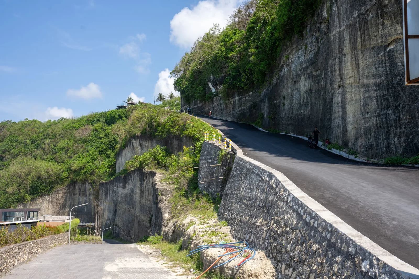Route étroite taillée dans une falaise calcaire du sud de Bali, avec un scooter à l'approche du virage