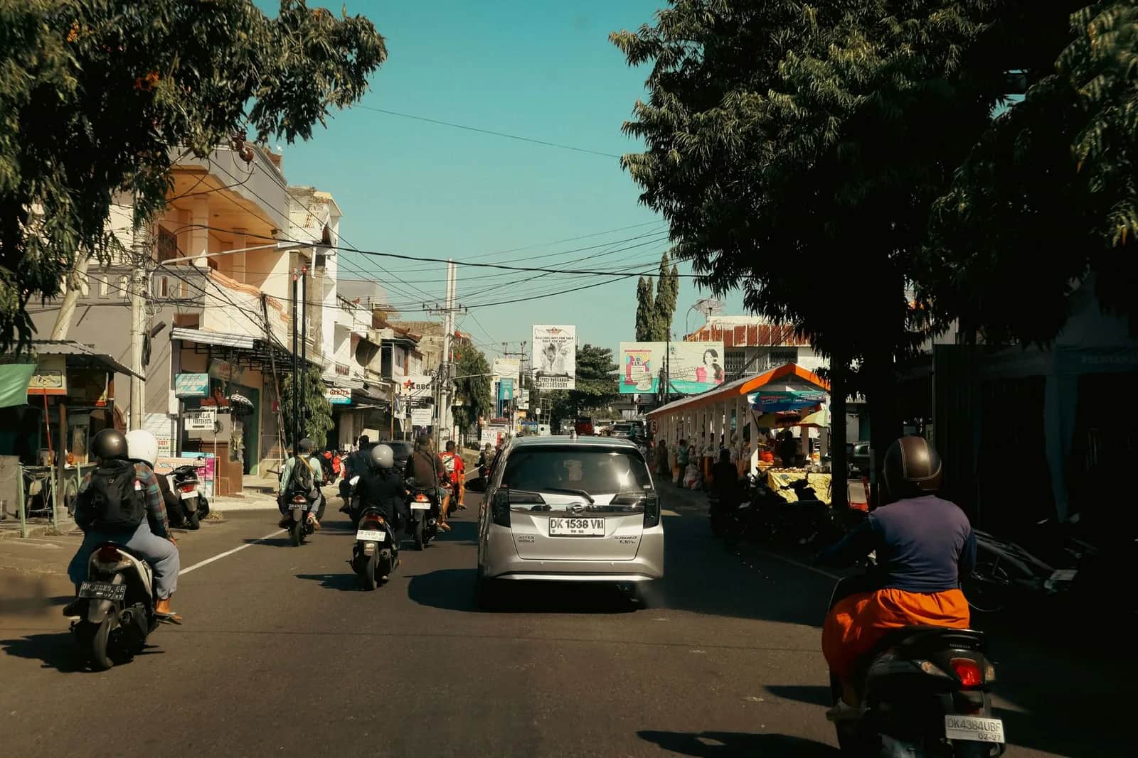 Voiture de location grise entourée de scooters dans une rue commerçante de Bali, en Indonésie
