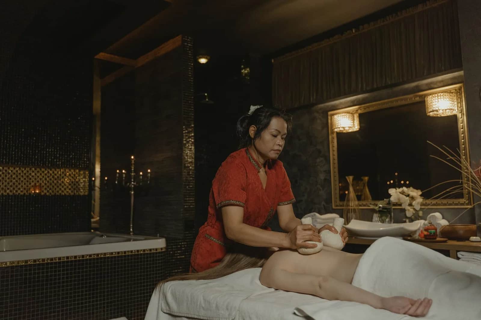Masseuse appliquant des compresses d'herbes chaudes lors d'un soin en cabine de spa à la lumière tamisée