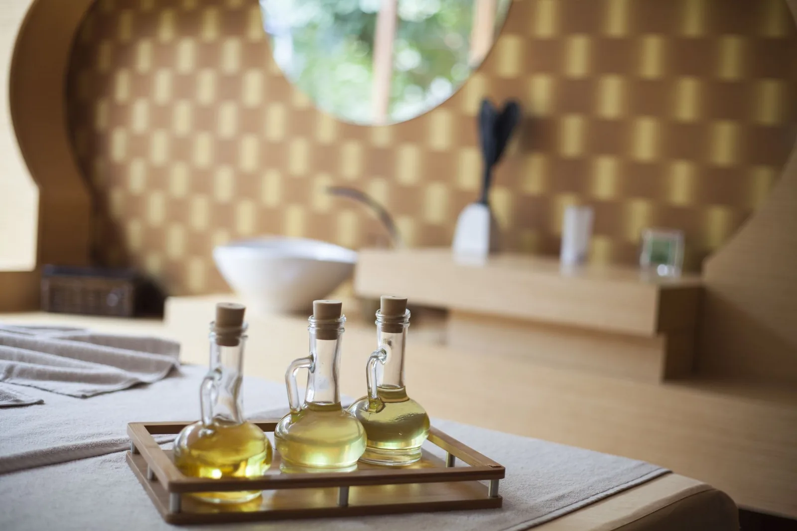 Flacons d'huile de massage posés sur un plateau en bois au bout d'une table de soin, dans une cabine de spa