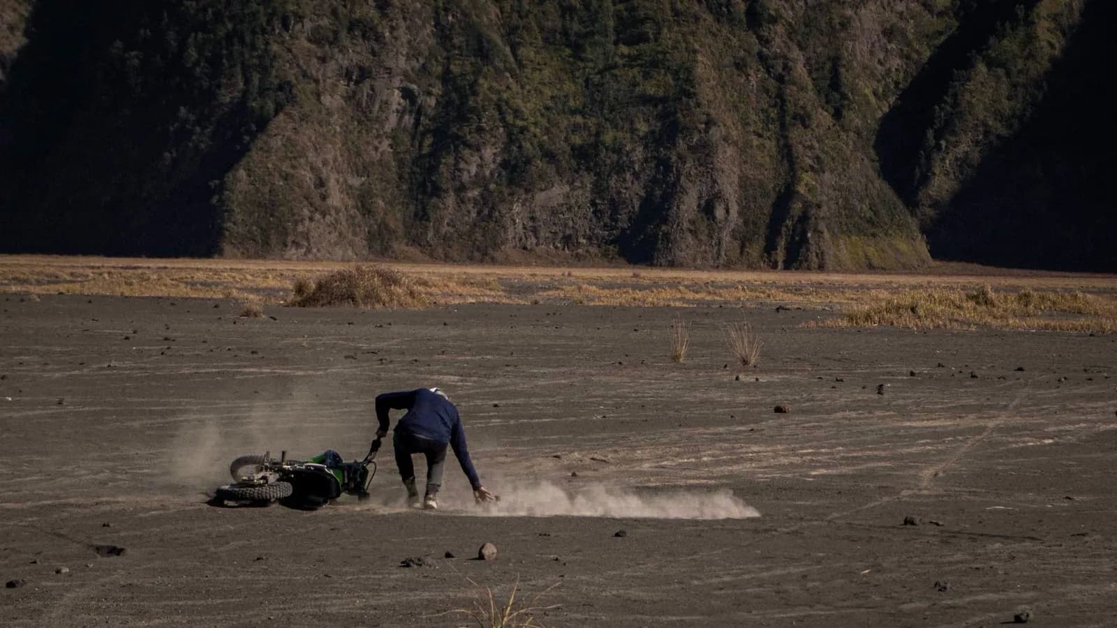 Pilote relevant sa moto tout-terrain sur une vaste plaine de cendre volcanique noire, au pied des parois d'une caldeira