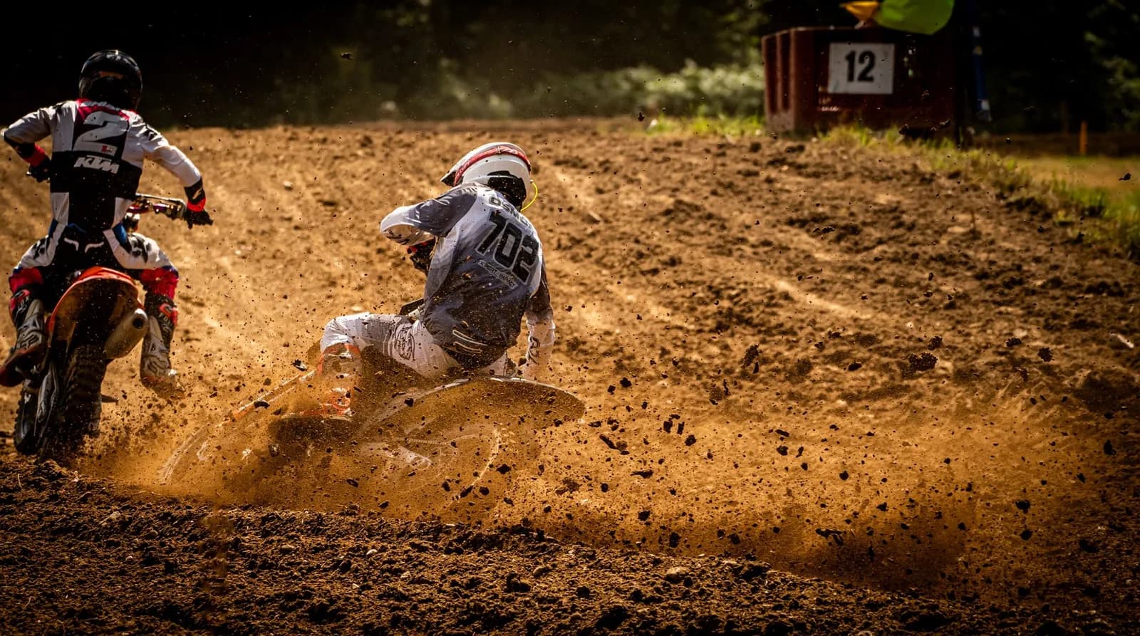 Deux pilotes de motocross en équipement complet projetant de la terre dans un virage sur une piste aménagée