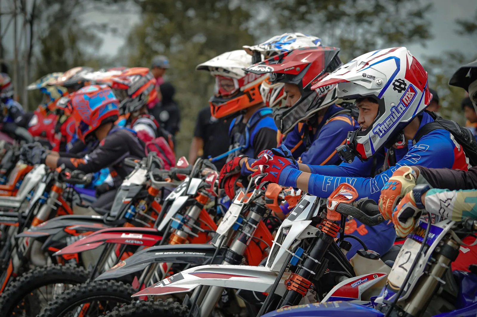 Groupe de pilotes en casque intégral, gants et maillots de motocross alignés sur leurs motos avant le départ, en Indonésie
