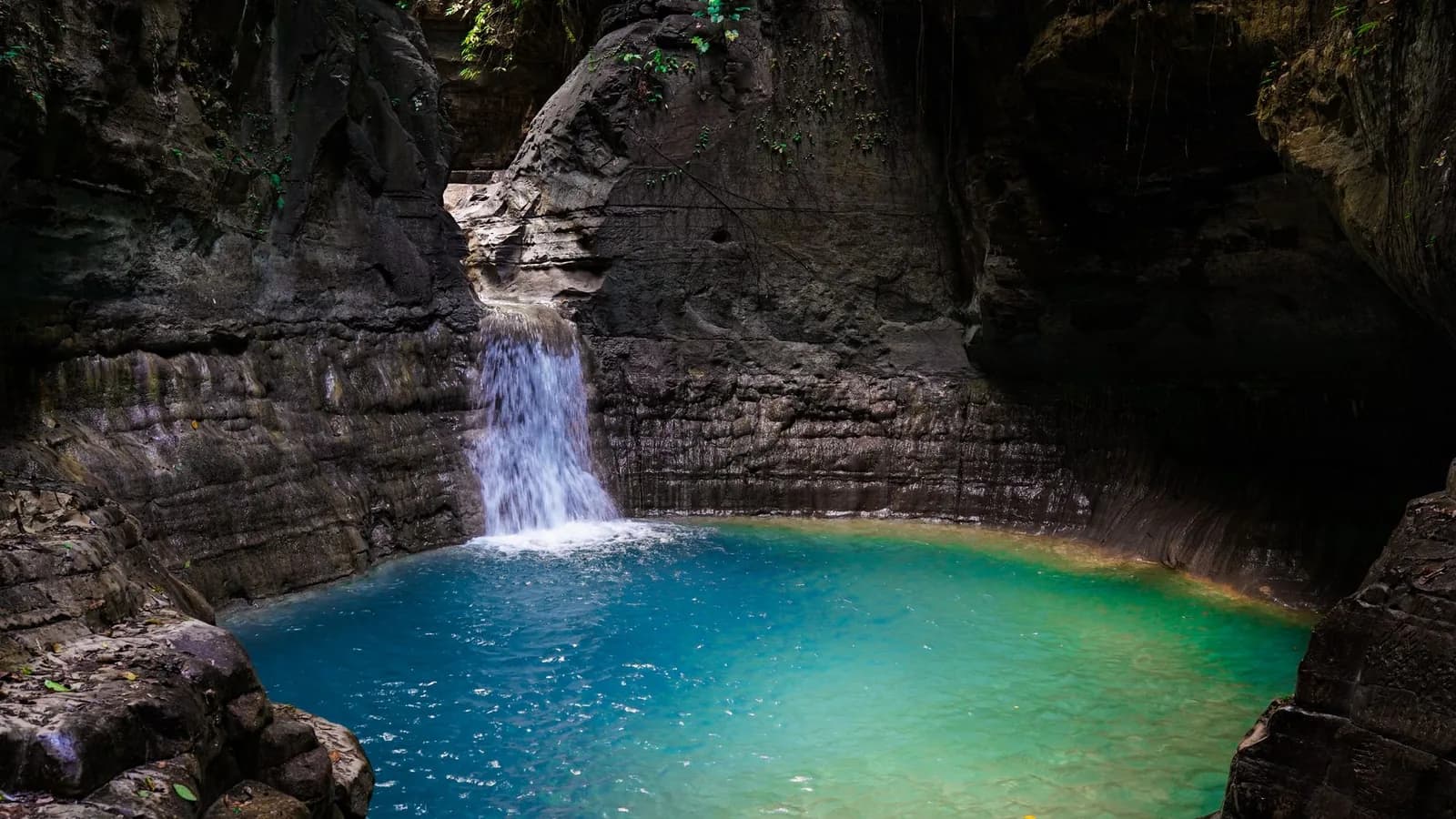 Cascade tombant dans un bassin d'eau douce turquoise encaissé entre des parois de roche stratifiée, dans une forêt tropicale indonésienne
