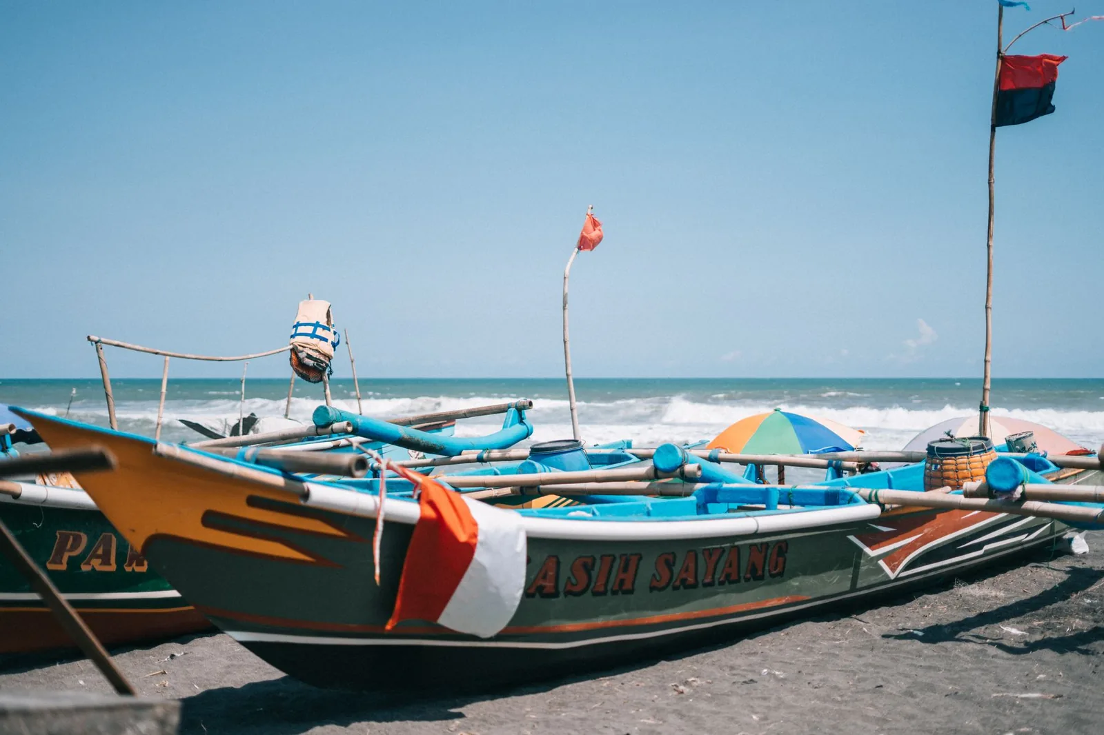 Jukungs de pêche à balancier aux coques peintes échoués sur le sable devant la mer, comme sur la plage du port de Padang Bai à Bali