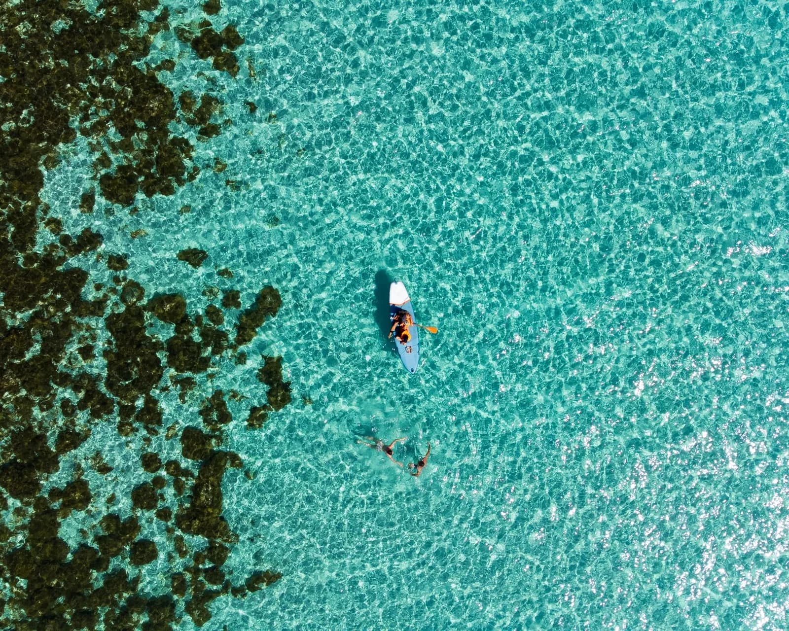 Vue aérienne de nageurs avec masque et tuba et d'un kayak au-dessus d'un récif dans une eau turquoise peu profonde, comme au Blue Lagoon de Padang Bai à Bali